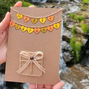 Handcrafted birthday card with a garland of colourful hearts against the backdrop of a waterfall.