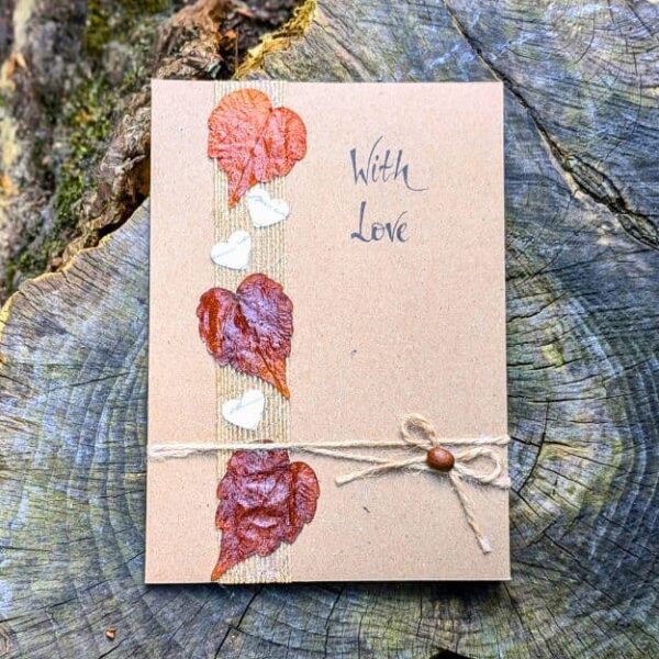 Handmade Valentine’s Day card with pressed leaves, natural twine, and handwritten “With Love” text, photographed on a wooden background.
