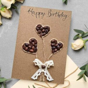 Handmade Greeting Card for Birthday with coffee bean hearts and a lace bow, set against a backdrop of roses and kraft paper.