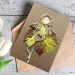 Best handmade romantic card for her shows a woman made of yellow feathers and leaves holding a wooden heart.