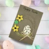Charming Handmade Easter Card - Let Spring Blossom Charming handmade Easter card featuring a colourful egg made of cardstock, accompanied by three flowers crafted from felt, paper, and coffee beans.