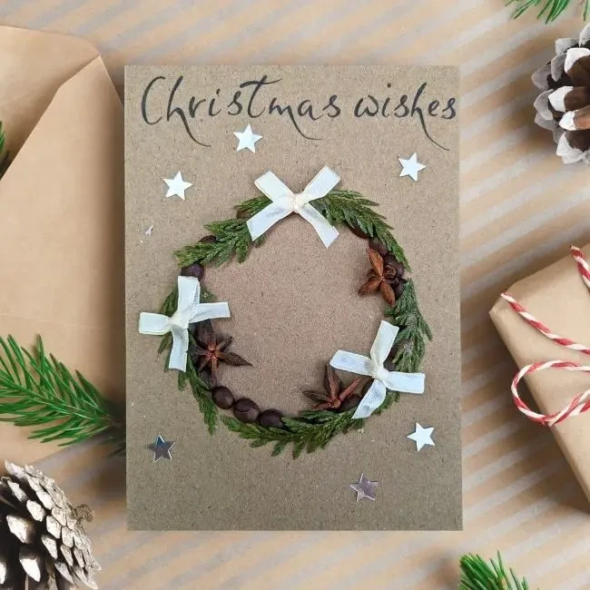 Handmade and Festive Wreath Christmas Card Design for Holiday Cheer image 1 Handmade Festive Wreath Christmas Card with foliage wreath, star anise, and ribbon on brown paper.