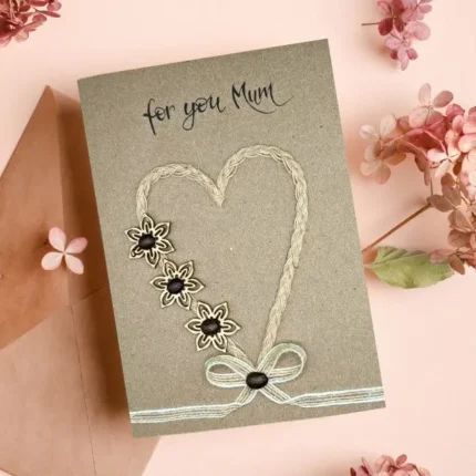 Handmade Thank You Mum card featuring a heart and flowers design in string, with "for you Mum" text. This heartfelt gift, perfect for any occasion, comes on an envelope adorned by pink dried flowers.