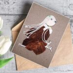 Handcrafted feather greeting card made of dry leaves, wood, and white cotton string, featuring a reindeer.