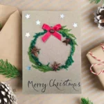 Personalised Handmade Christmas card on brown paper, displaying festive wreath and red ribbon bow.