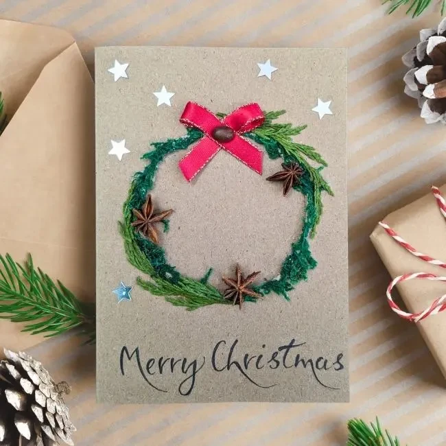 Personalised Handmade Christmas Card with Festive Wreath image 1 Personalised Handmade Christmas card on brown paper, displaying festive wreath and red ribbon bow.