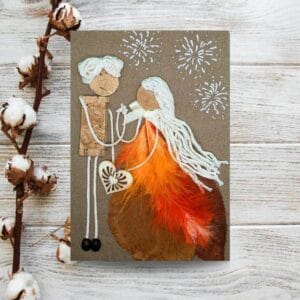Crafted card with stick figures, perfect for the Handmade Anniversary Cards category image. Figures are adorned with bark, yarn, and feathers, holding a heart.