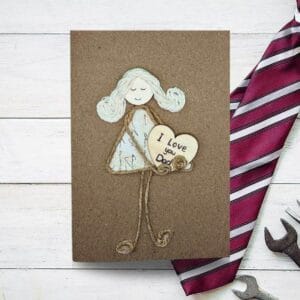 Handmade Father's Day card featuring a girl holding a heart and a tool, symbolizing love and craftsmanship.
