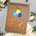 Beautiful Handmade Happy 50th Birthday Cardfeaturing two cork dogs holding colourful balloons on recycled kraft paper, personalised eco-friendly card for dog lovers.