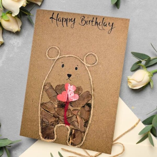 Handmade bear birthday card made from kraft paper with a twine outline and red heart balloons.