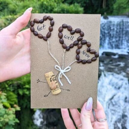 Handmade get well soon card decorated with real coffee beans shaped into balloon designs, tied with natural string on kraft card.