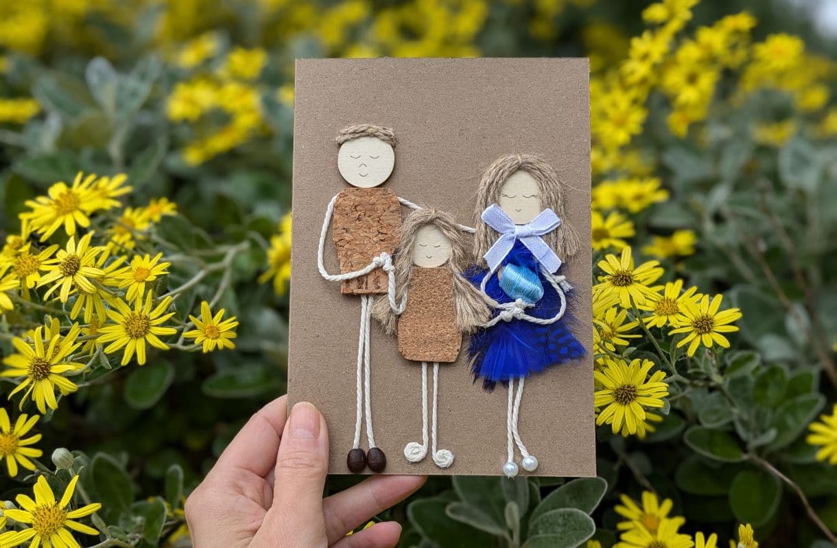 Cork in handmade card featuring a family design made from cork, twine, and natural materials, photographed outdoors among yellow flowers.