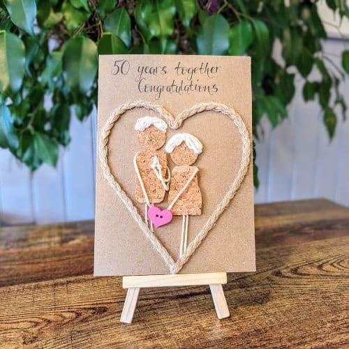Cork in handmade card showing an anniversary design with a couple made from cork, twine heart detail, and handwritten “50 years together” message.