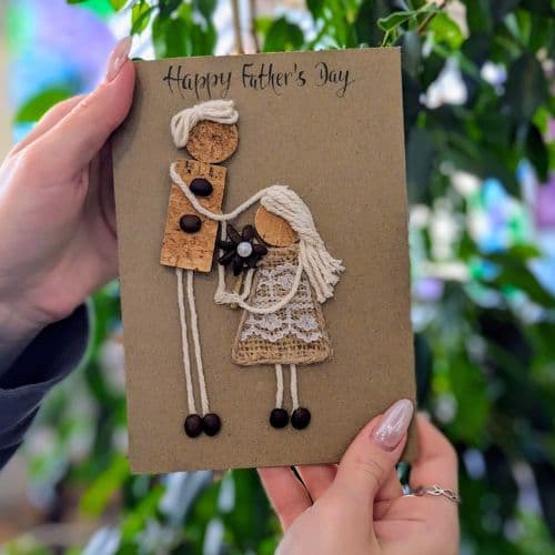 Cork in handmade card featuring a Father’s Day design with cork figures, twine hair, lace detail, and natural embellishments.