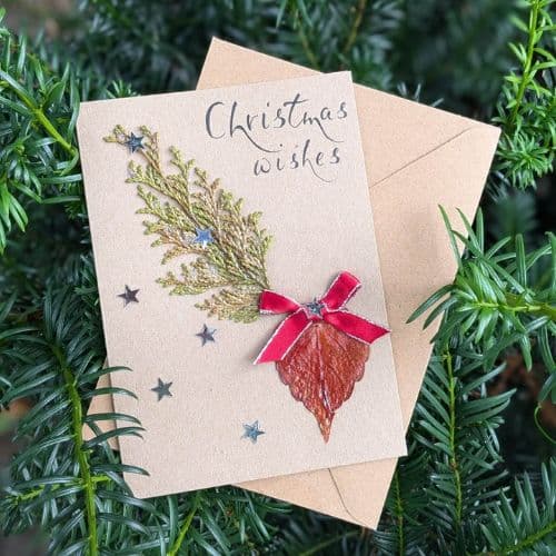 Dry leaves in handmade cards featuring a Christmas wishes design with a natural leaf, red ribbon, evergreen sprig, and kraft envelope