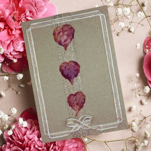 Dry leaves in handmade cards arranged as three heart shapes on a handmade heart card with stitched detailing and Kraft paper.