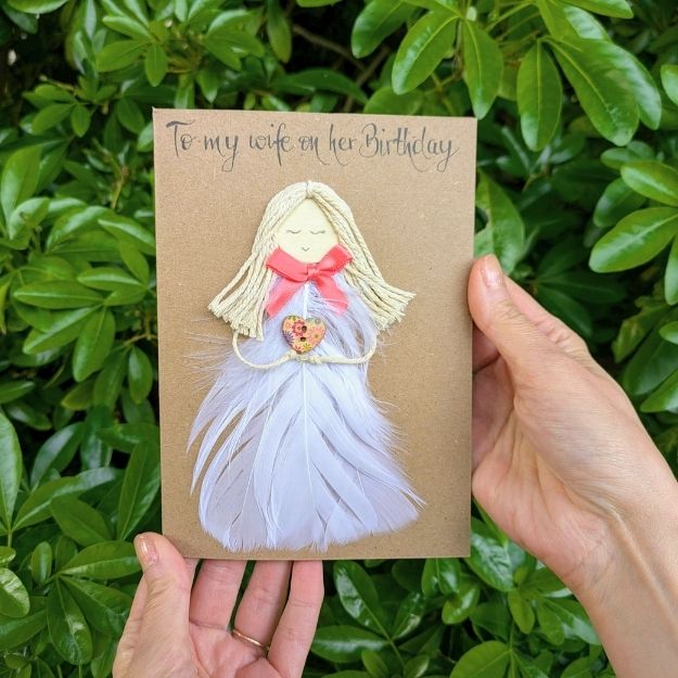 "To my wife on her Birthday" kraft card featuring an angel figure made from luxury handmade card materials, including white feathers for the dress, cotton twine hair, and a floral heart button.