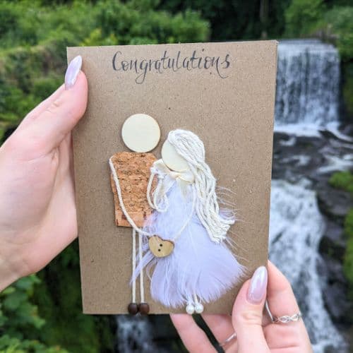 Types of greeting cards – handmade engagement card on kraft paper featuring a couple with feather details and natural materials.