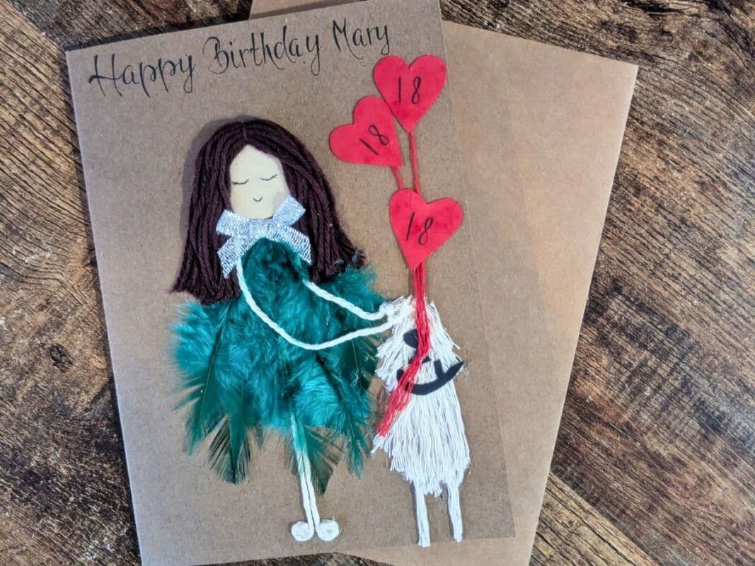 Handmade 18th birthday card for Mary featuring a figure with a green feather dress and a white yarn dog, reflecting the quality and cost of a handmade card.