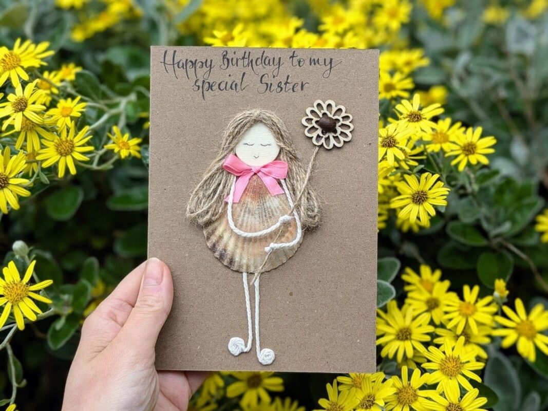 Handmade birthday card for a sister featuring a scallop shell dress, pink bow, and handmade calligraphy, demonstrating the premium quality and cost of a handmade card.